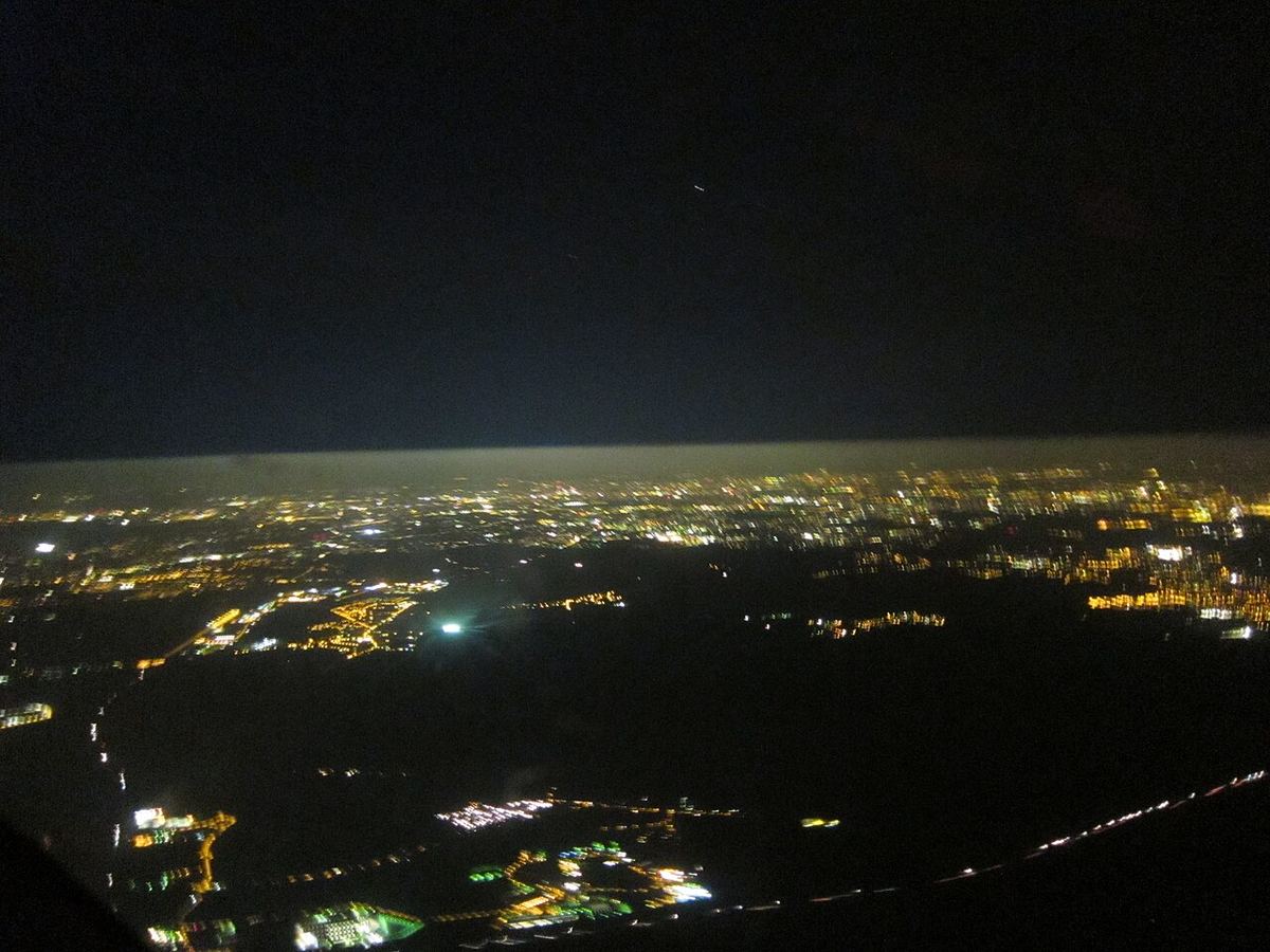 Luzes de uma cidade vistas de um monte à noite com o céu alaranjado pelo brilho artificial