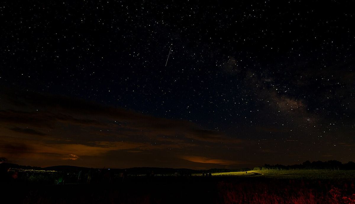 Grupo de observadores sob um céu estrelado com a Via Láctea ao anoitecer
